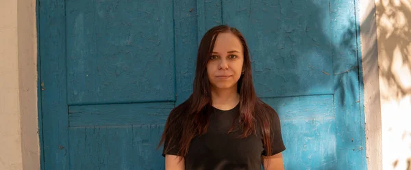 Eine junge Frau in einem schwarzen T-Shirt mit langen Haaren vor dem Hintergrund eines alten Gebäudes mit blauen Türen. — Stockfoto