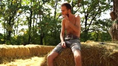 Sakallı genç yakışıklı bir adam samanlıkta çıplak bir şekilde uzanıyor ve sigara içiyor..