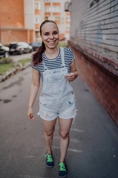 Uma jovem mulher em roupas casuais está e sorri na rua no verão. — Fotografia de Stock