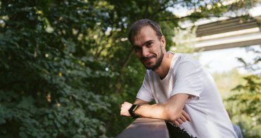 Parktaki yeşil ağaçların arka planında sakallı yakışıklı bir adamın portresi..