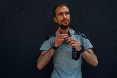 Sıradan giysiler içinde sakallı genç yakışıklı bir adam sokak duvarına karşı poz veriyor.