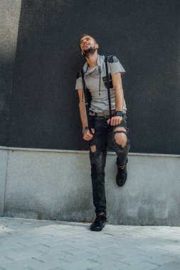 Sıradan giysiler içinde sakallı genç yakışıklı bir adam sokak duvarına karşı poz veriyor.