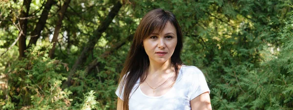 Un retrato de una guapa mujer sobre el fondo de los árboles verdes del parque.. — Foto de Stock