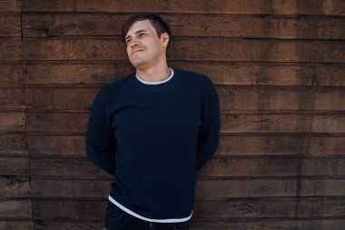 Mavi kazaklı yakışıklı bir adam tahta arka planda poz veriyor.