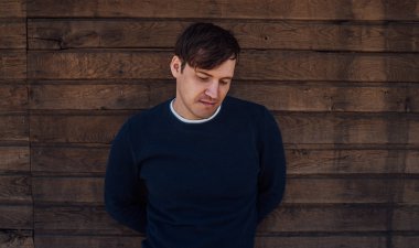 Mavi kazaklı yakışıklı bir adam tahta arka planda poz veriyor.