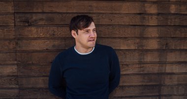 Mavi kazaklı yakışıklı bir adam tahta arka planda poz veriyor.