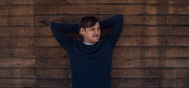 Mavi kazaklı yakışıklı bir adam tahta arka planda poz veriyor.