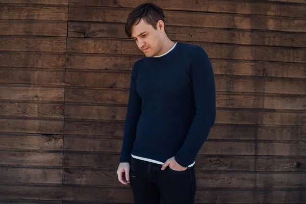 Un hombre guapo en un jersey azul se coloca sobre un fondo de madera. — Foto de Stock