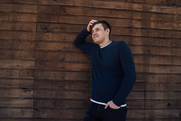 A handsome man in a blue sweater poses against a wooden background — Stock Photo, Image