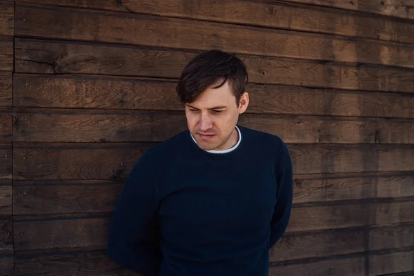 Mavi kazaklı yakışıklı bir adam tahta arka planda poz veriyor.