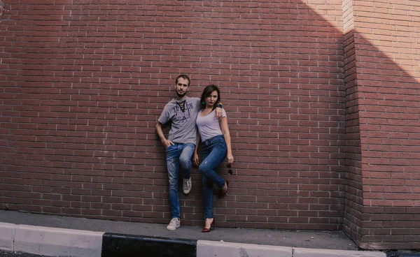 Una joven pareja amorosa con camisetas y pantalones vaqueros se enfrenta a una pared de ladrillo.. —  Fotos de Stock