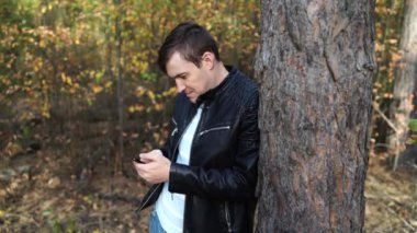 Caddedeki deri ceketli adam, akıllı telefondan mesaj yazıyor. Telefonu olan adam.