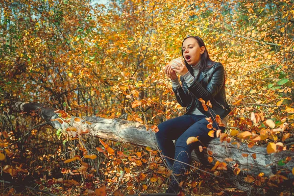 Женщина питается в солнечном весеннем парке. Молодая женщина с солнечным днем ест гамбургер в осеннем лесу. — стоковое фото
