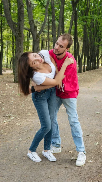 開花木や低木の背景に愛の抱擁とポーズのカップル。開花公園の背景に若い男と女の子 — ストック写真
