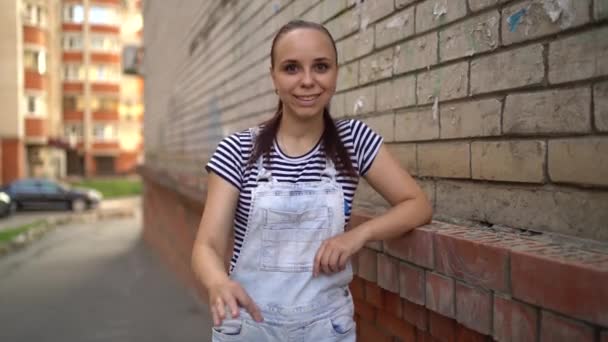 Μια νεαρή γυναίκα με casual ρούχα χαμογελά και δείχνει το σημάδι του OK στέκεται στην πόλη — Αρχείο Βίντεο
