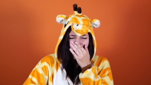 Uma jovem bonita em um grande pijama de girafa está gritando de cansaço em um fundo laranja no estúdio. — Vídeo de Stock