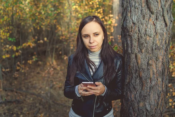 A mulher usa um smarphone na floresta de outono. Feminino disca uma mensagem no telefone — Fotografia de Stock