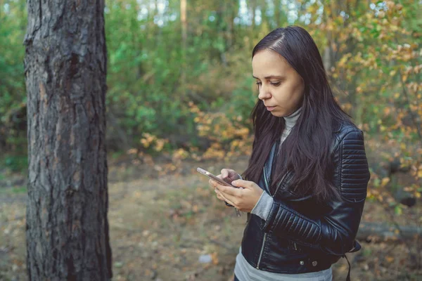 A nő okostelefont használ az őszi erdőben. A nő tárcsáz egy üzenetet telefonon. — Stock Fotó
