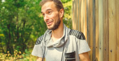 Parktaki yeşil ağaçların arka planında sakallı yakışıklı bir adamın portresi..