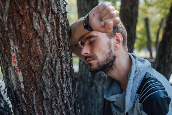 Portret przystojnego mężczyzny z brodą, leżącego ramię na drzewie z zamkniętymi oczami w parku.. — Zdjęcie stockowe