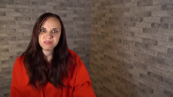 Una joven con un hoodie rojo resenta y expresa sus emociones negativas sobre un fondo de ladrillo.. — Vídeos de Stock