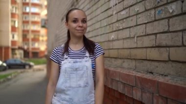 Gündelik giysiler içinde genç bir kadın gülümsüyor ve sokakta dikilmiş iyi bir izlenim veriyor..