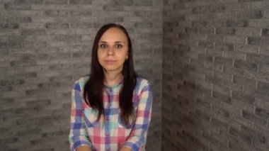 Ekose gömlekli güzel genç bir kadın gri tuğlalı arka planda geziniyor..