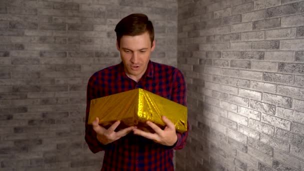Sad handsome man received the wrapped gifts and began to smile broadly. Happy man holds presents against the background of a gray brick wall. The concept of Holiday, holiday discounts, gifts and sales — Stock Video