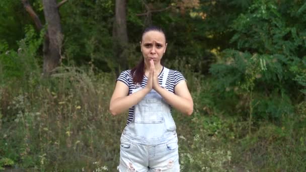 A young woman in casual clothes is begging for something in the forest. — Stock Video