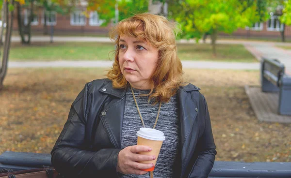 Mulher adulta bebendo café no Parque do Outono, sentado em um banco — Fotografia de Stock