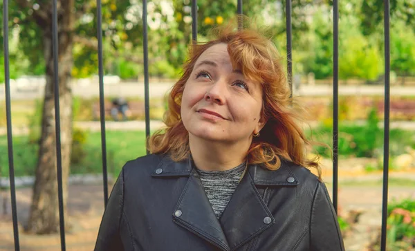 Mujer contra valla en el jardín. Mujer contenta que se ve enamorada mientras se encuentra en un parque verde contra la valla ornamental de hierro. — Foto de Stock