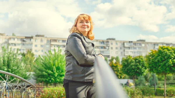 Verlegen vrouw leunend op handgreep in de tuin. Charmante mooie vrouw bedachtzaam kijkend naar camera aanraken haar in zonnige dag in groen park — Stockfoto