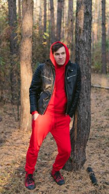 Güneşli bir günde ağaçların yanında duran adam. Ağaçların arasında poz veren gündelik kıyafetler giyen genç adamın portresi