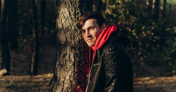 Man standing beside trees in sunny day. Portrait of young man in casual clothes posing among trees — Stock Photo, Image