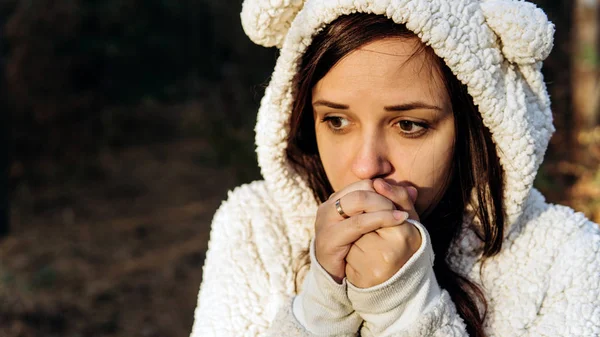 白いふわふわのパーカーを着た若い女性が森の中の寒さから縮みます. — ストック写真