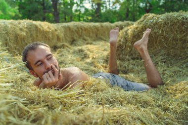 Samanlıkta bir adam, samanlıkta bir erkek. Saman balyasında oturan adam. Genç adam saman balyasında yatmaktan hoşlanıyor.