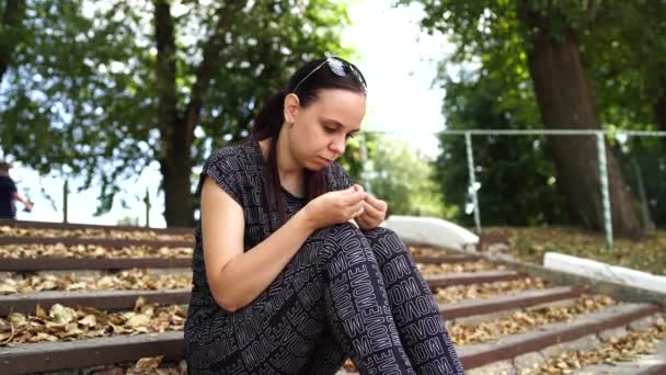 Zamyšlená žena v černé teplákové soupravě sedí na schodech s spadlým listím v parku. — Stock video