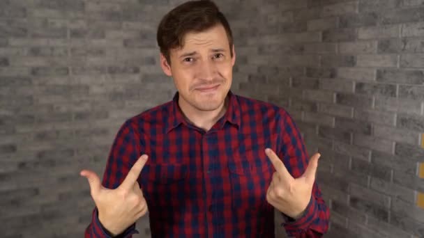Ein junger gutaussehender Mann im karierten Hemd zeigt ihre Hände auf einem grauen Backsteinhintergrund. — Stockvideo