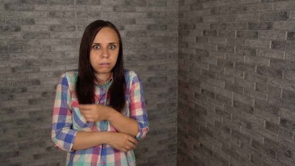 Una giovane donna in una camicia plaid mostra una paura su uno sfondo di mattoni. Una donna era afferrata dalla paura. — Video Stock