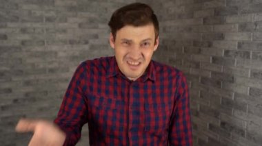 Ekose gömlekli genç yakışıklı bir adam facepalm yapıyor. Şokta olan adam yüzünü gri tuğladan bir arka planda avuç içi ile kapatıyor..