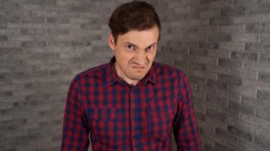 Ekose gömlekli genç bir adam stüdyodaki gri tuğlalı arka planda bir şeye kızmış..