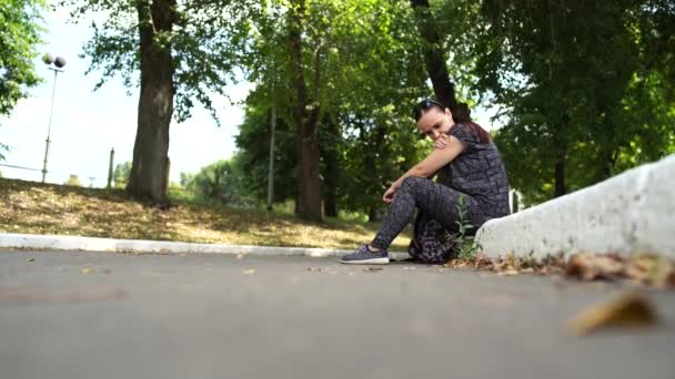 Een mooie jonge vrouw in een sportpak met lang haar zit op de stoep en kijkt bedachtzaam in de verte. — Stockvideo