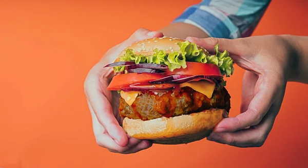 Women's hands are holding a huge juicy hamburger on orange backg — Stock Photo, Image