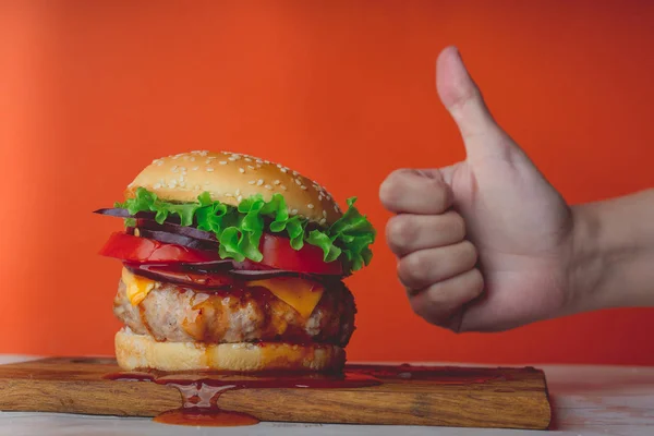 Kesme tahtasının üzerinde kocaman sulu bir hamburger var. Kadının elinde benzer bir işaret var. Onaylı abur cubur konsepti.