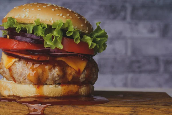 Büyük, sulu bir hamburger, gri tuğlalı arka planda bir doğrama tahtasının üzerinde..