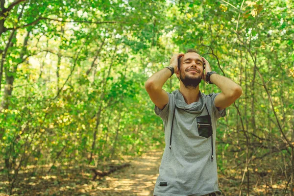 El tío está disfrutando de un paseo por el Parque. Un hombre experimenta éxtasis, de pie en los bosques y sosteniendo la cabeza. Hipster sonríe y disfruta — Foto de Stock