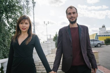 Mutlu çift. Şehirde yürüyüş yapmak. Genç çift uzun elbiseli bir kadını kucağında tutuyor. Güzel, şık bir çift Avrupalı şehrin sokaklarında yürüyor..