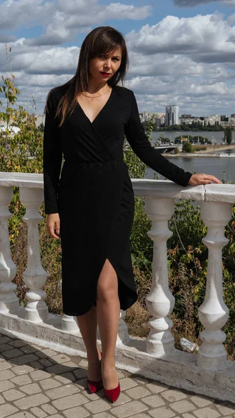 Красивая женщина в черном платье стоит на набережной летом. — стоковое фото