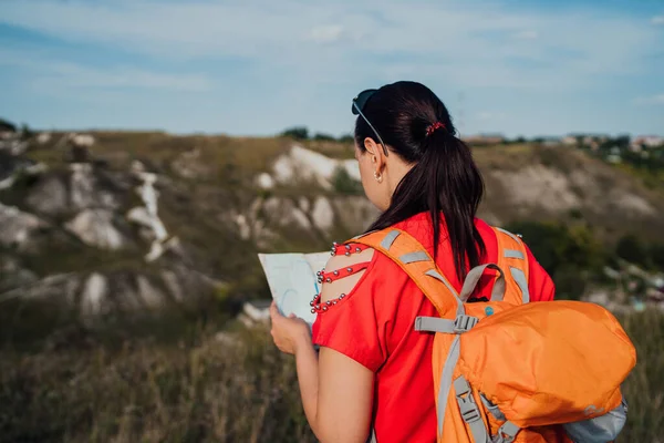 Traveling woman with map in nature. Woman with backpack walking in narrow winding path going through green bushes and trees. Casual woman carrying backpack. Traveler traveling alone — Stock Photo, Image