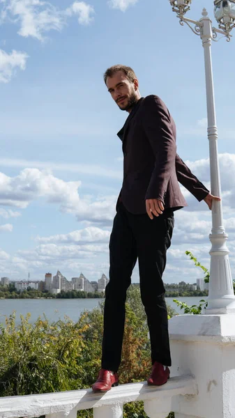 Um homem bonito novo com barba da construção slim no terno está posando em uma cerca branca do dique. — Fotografia de Stock